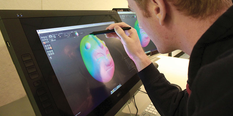Male student uses stylus to create 3-D render of a multicolor face,Digital Media and Design
