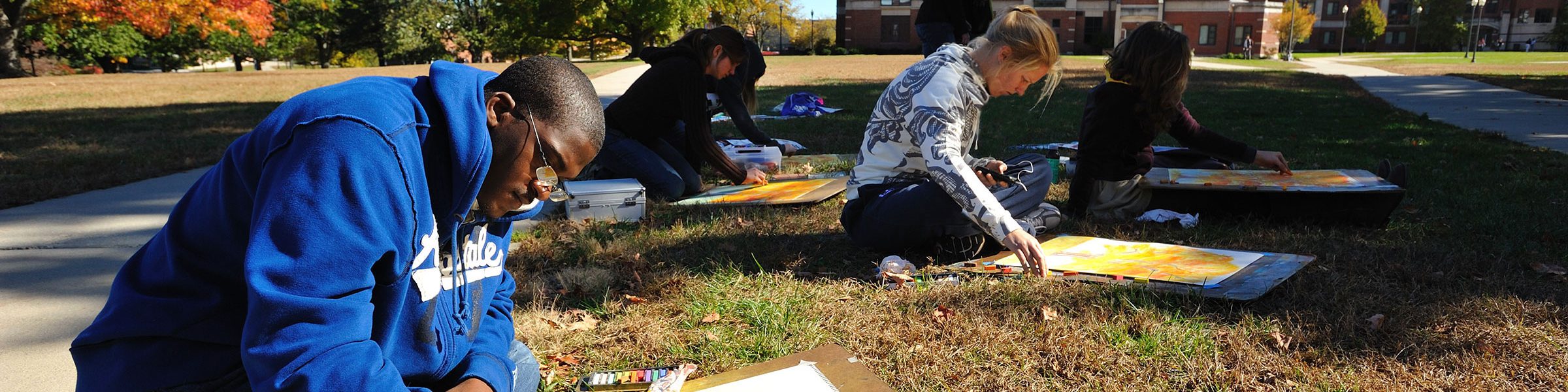 Four UConn Art & Art History students sitting and working with pastels in the south quad lawn during the Fall