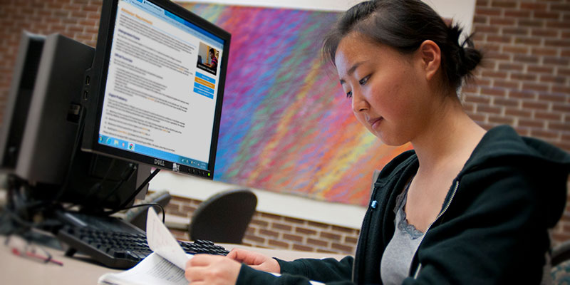 Graduate student sits and reads article with computer in front her and a multi-colored background