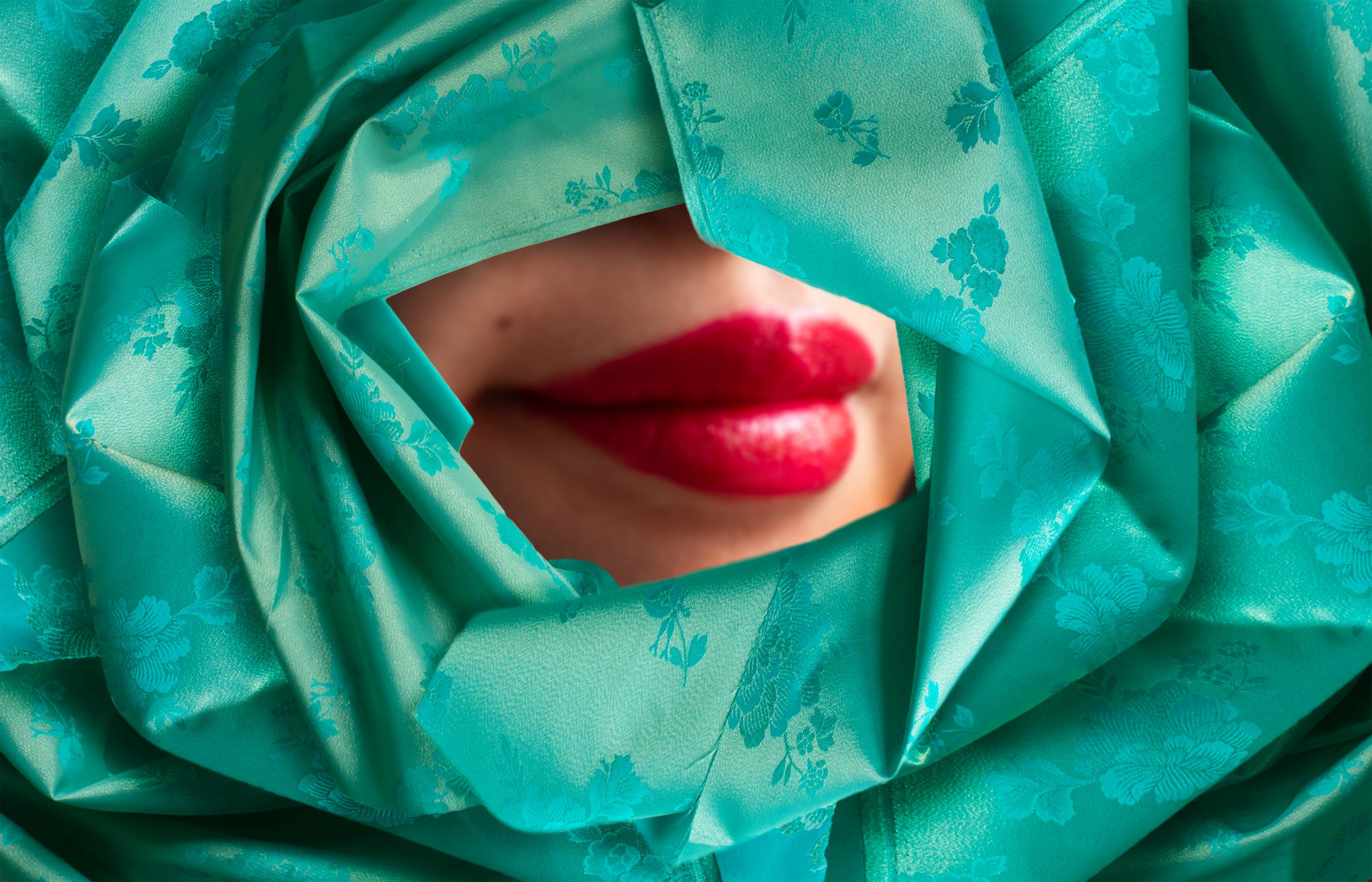 photograph of a pair of lips wearing bright red lipstick, framed by seafoam green origami 