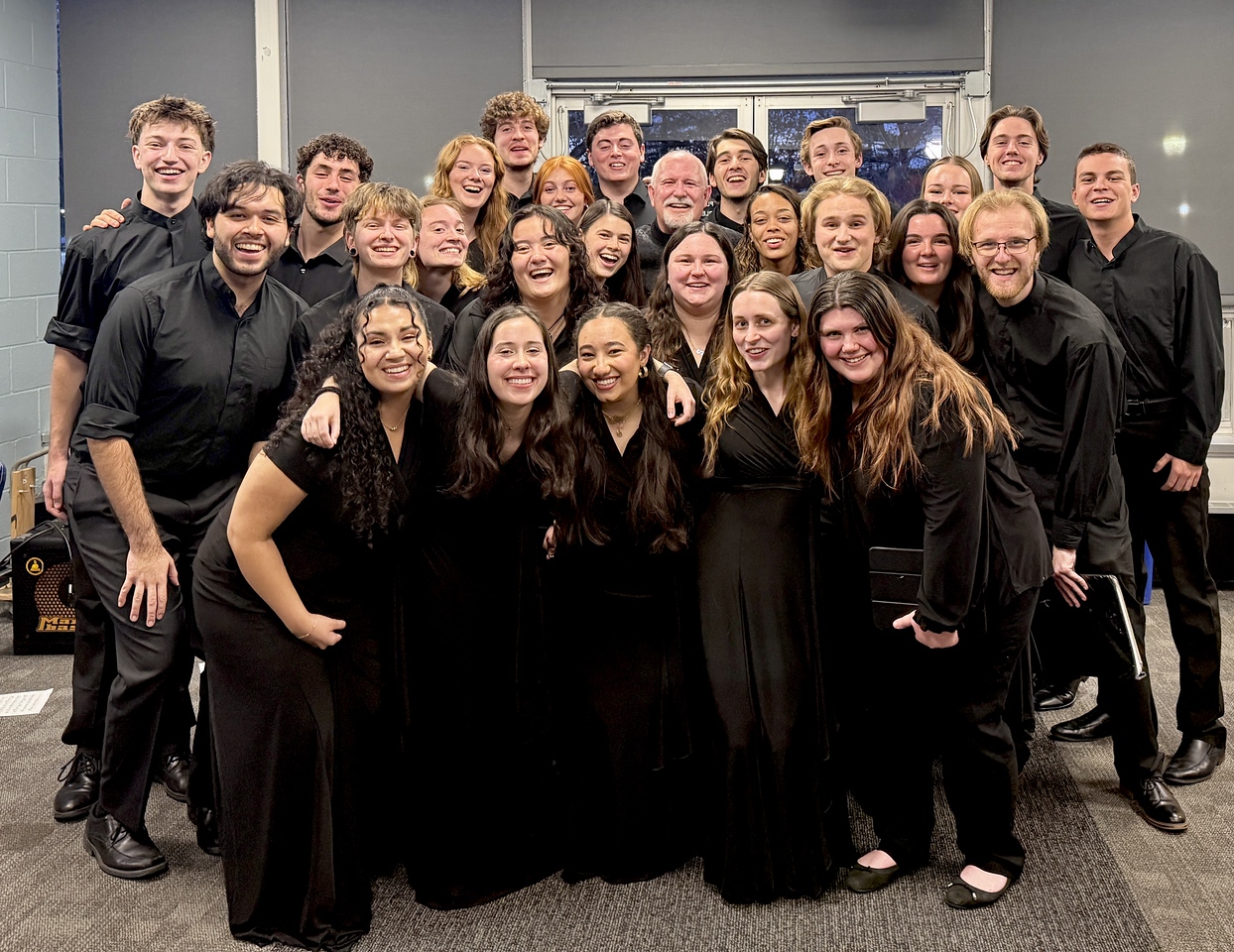 UConn Chamber Singers - a group of roughly 20 students gathered close and smiling in concert black attire